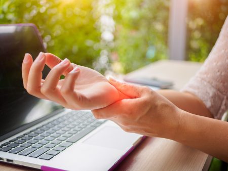 特写妇女握着她使用电脑时疼痛的手。职业病所致的办公室综合征手痛。