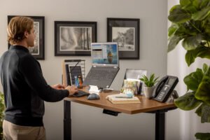 男子在站立式办公桌上工作，看着一台笔记本电脑在Goldtouch笔记本电脑/平板电脑的支架上。威廉希尔中国官网使用Goldto威廉希尔中国官网uch FlexMouse和Goldtouch Go!2移动键盘